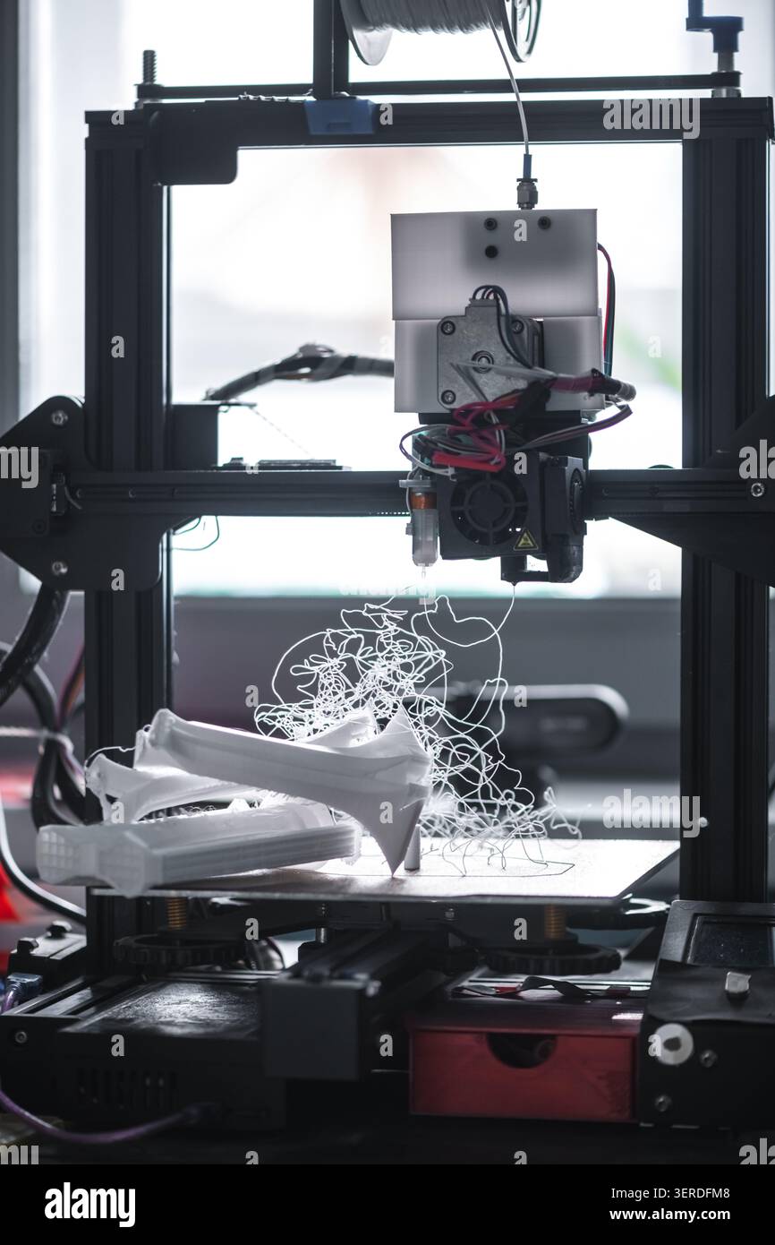 3D-Drucker funktioniert, wodurch bei teilweise geformten Modellen ein verworrenes weißes Kunststofffilament auf der Bauplatte entsteht, das einen technischen Fehler oder Fehler veranschaulicht Stockfoto