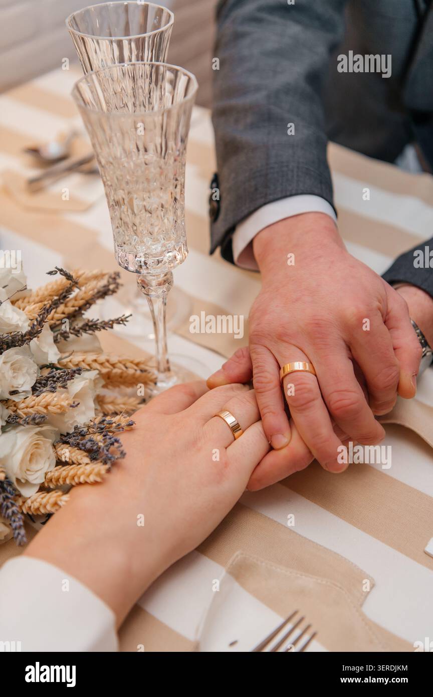 Eine zarte Nahaufnahme eines frisch vermählten Paares, das Hände hält und ihre goldenen Eheringe zeigt. Stockfoto