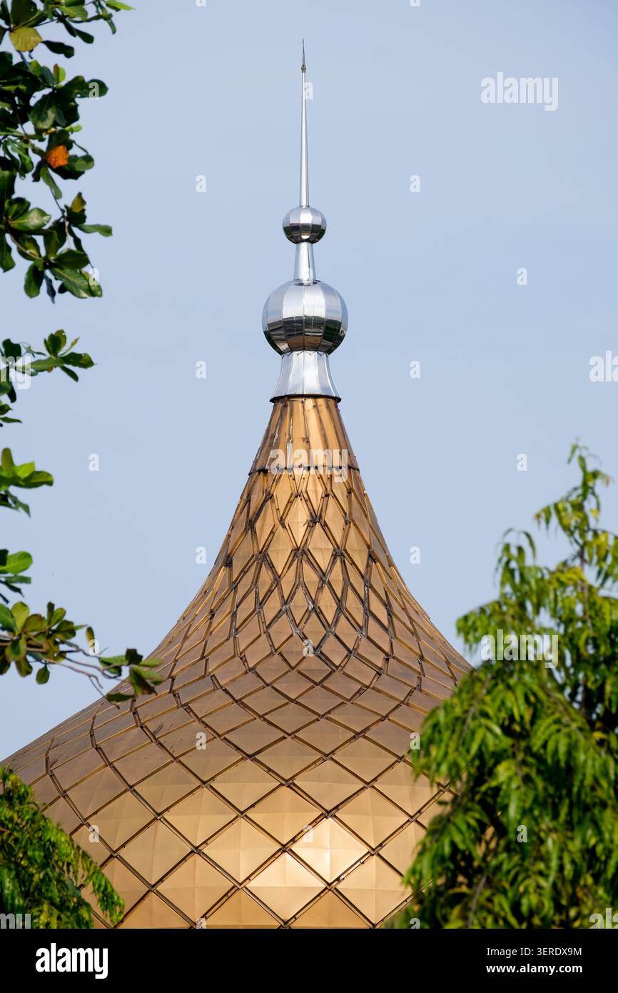 Nahaufnahme einer goldenen Moschee-Kuppel mit Edelstahlturm, der von grünen Bäumen vor klarem Himmel umgeben ist Stockfoto