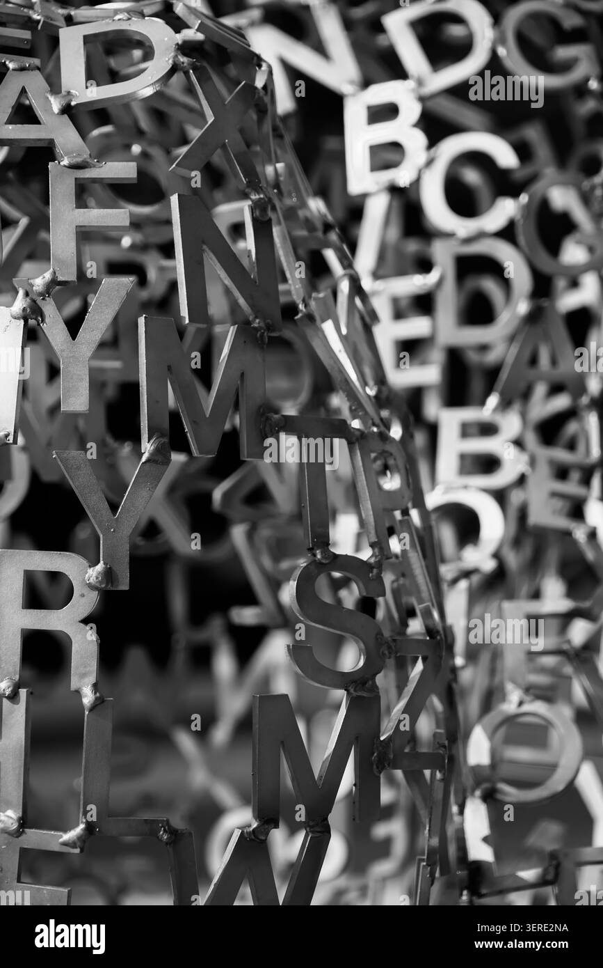 Eine abstrakte Schwarz-weiß-Nahansicht zahlreicher miteinander verflochtener Metallbuchstaben, die eine komplexe künstlerische Skulptur bilden. Die metallische Textur und die Komplexität Stockfoto
