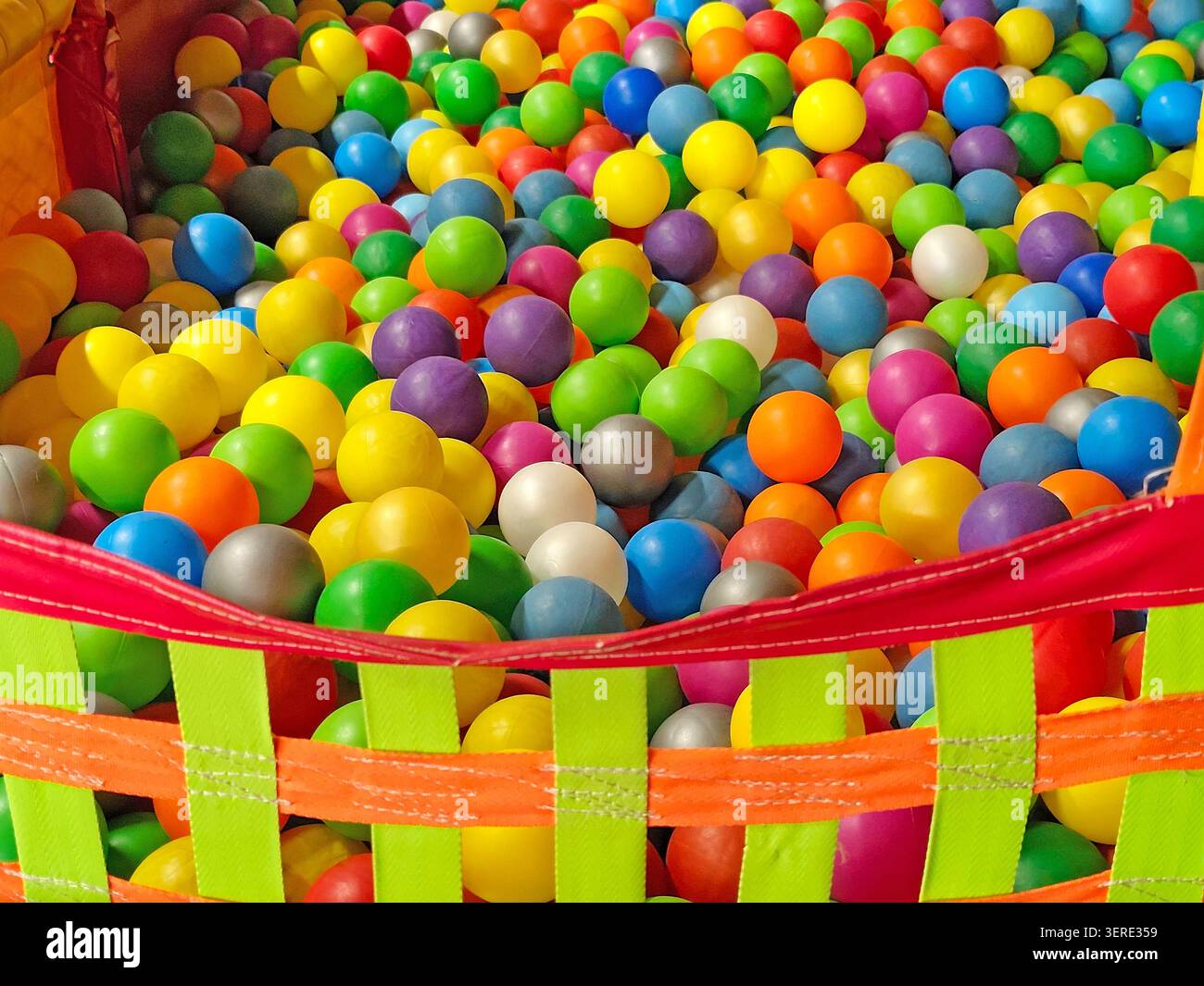 Bunte Plastikbälle füllen eine Kinderbällewanne in einem Indoor-Spielplatz. Helle mehrfarbige Kugeln schaffen einen lebendigen Vollbildhintergrund mit Stockfoto