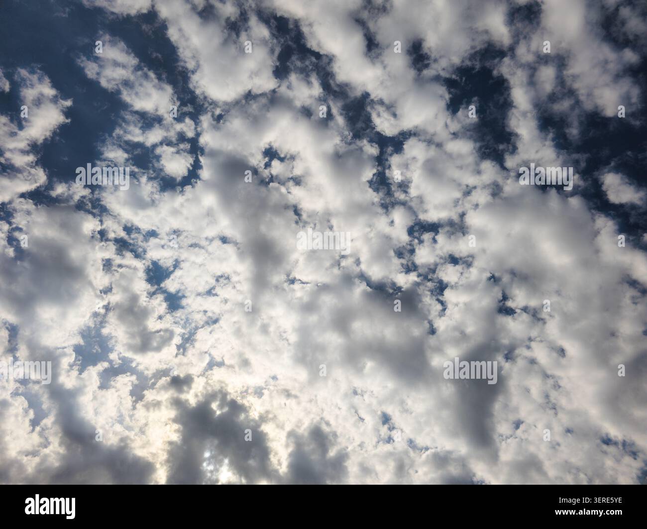 Weite Himmelsfläche mit weißen und grauen Wolken gegen tiefblaues Blau. Sonnenlicht wird durchfiltert und erzeugt dramatische Schatten und Lichter. Stockfoto