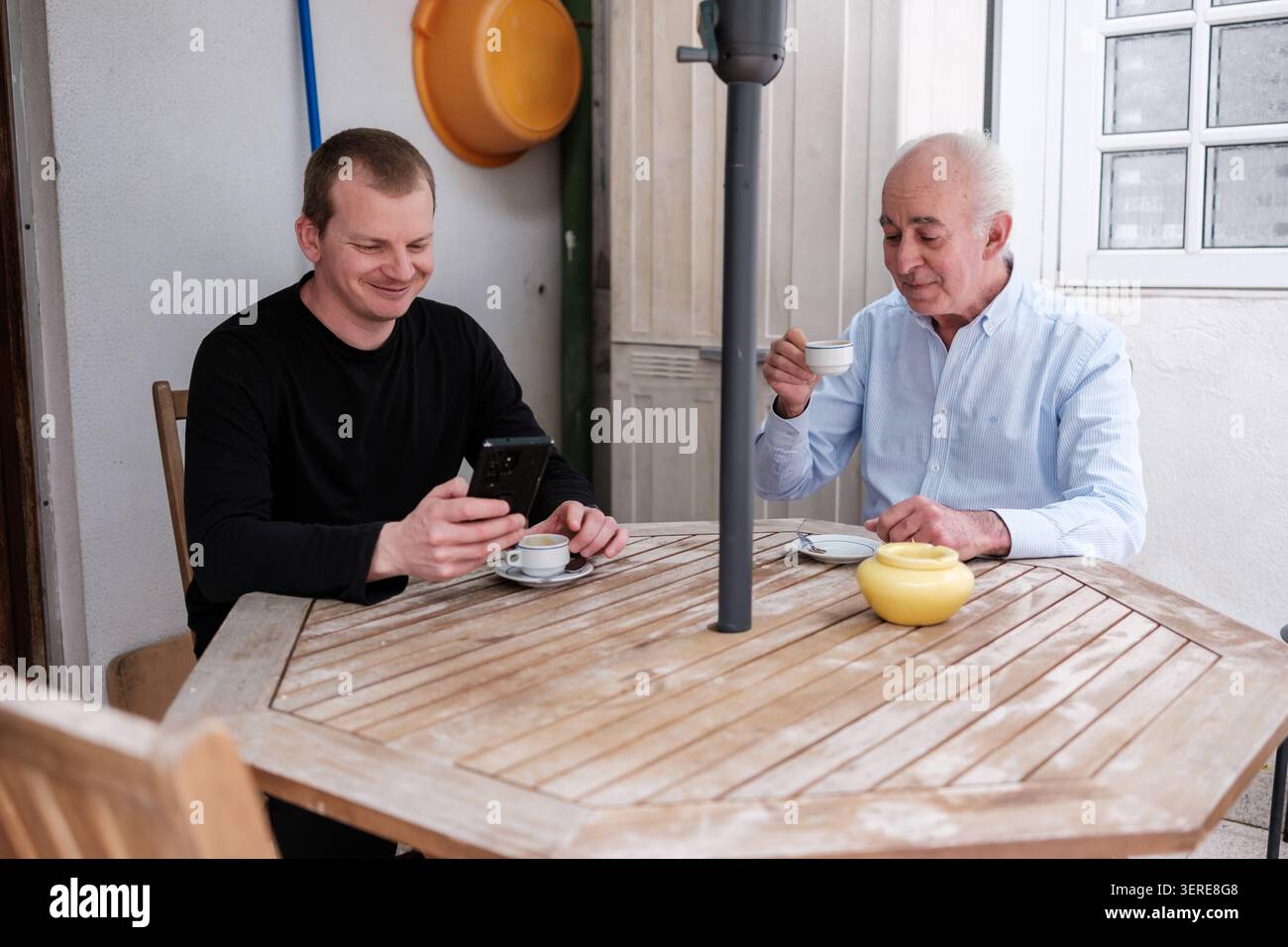 Erwachsene und ältere Männer teilen sich einen Moment mit Kaffee und Technologie draußen Stockfoto