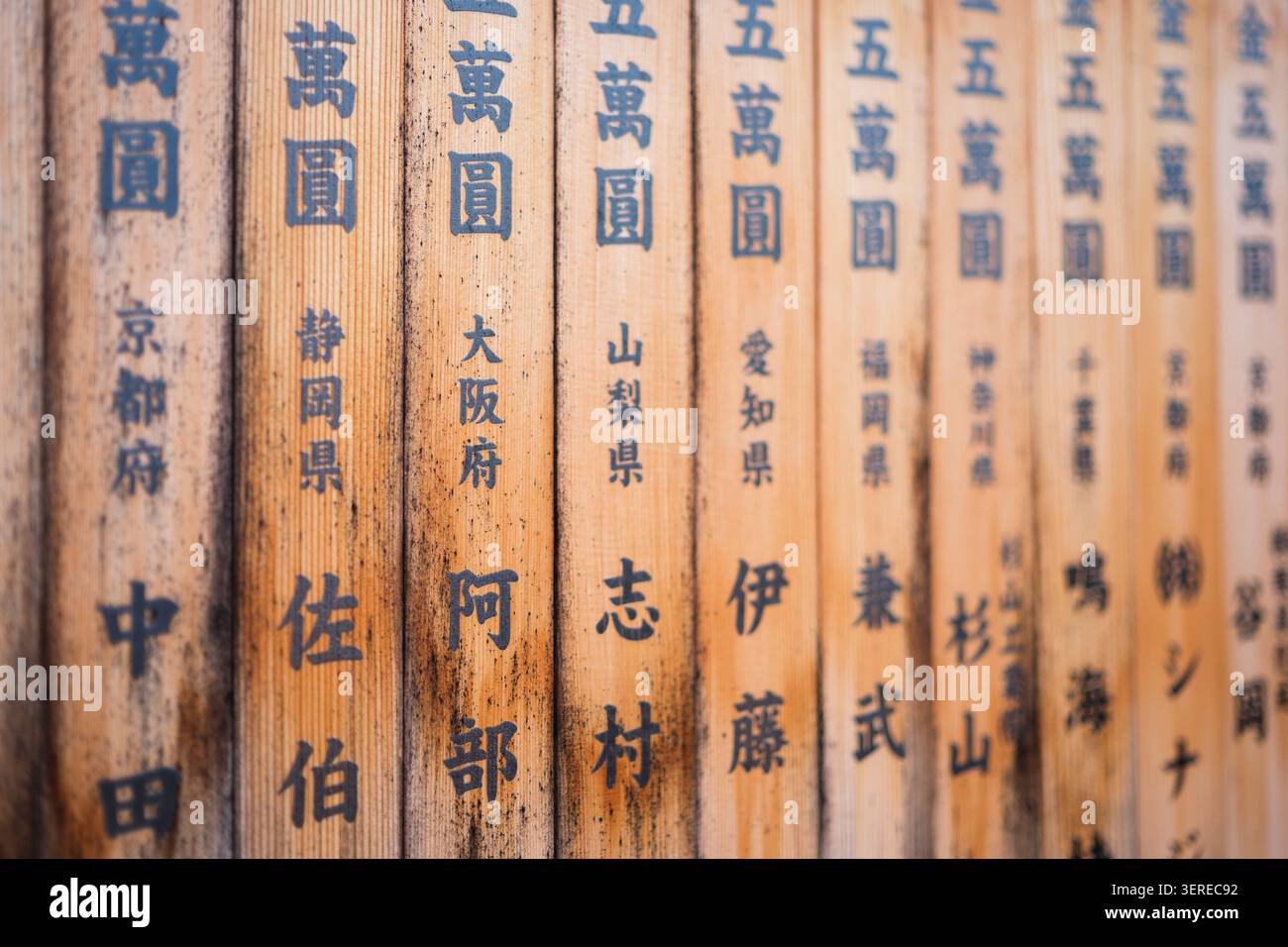 Verwitterte vertikale Holzbretter mit handgemalten schwarzen Kanji-Textnamen an einem traditionellen japanischen Schrein in Kyoto, Japan Stockfoto