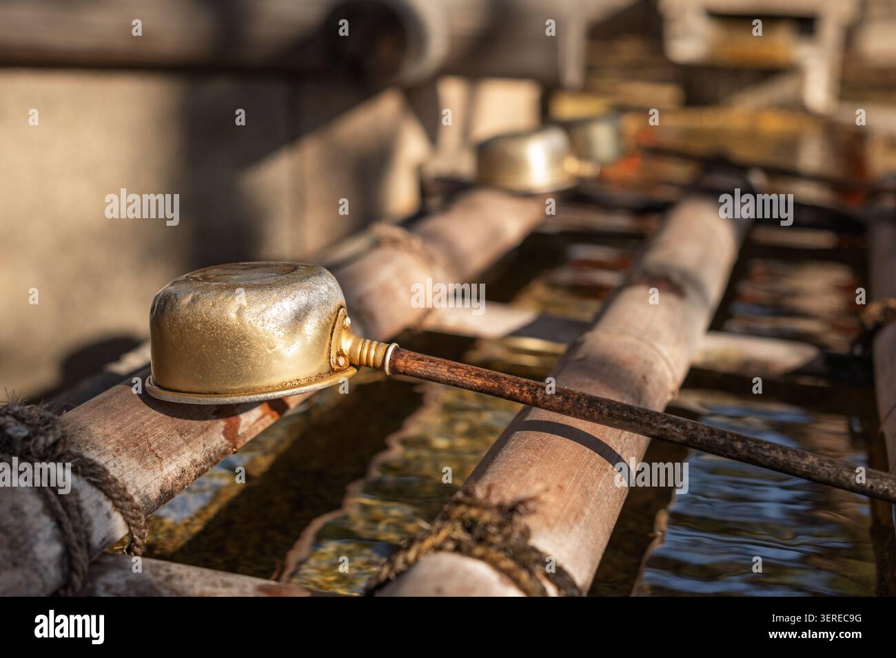 Eine Hishaku-Kelle aus Metall liegt über den Bambusschienen einer Chozuya, deren abgenutzte Oberfläche und einfache Form leise über dem stillen Wasser sitzt, Kyoto, Japan Stockfoto