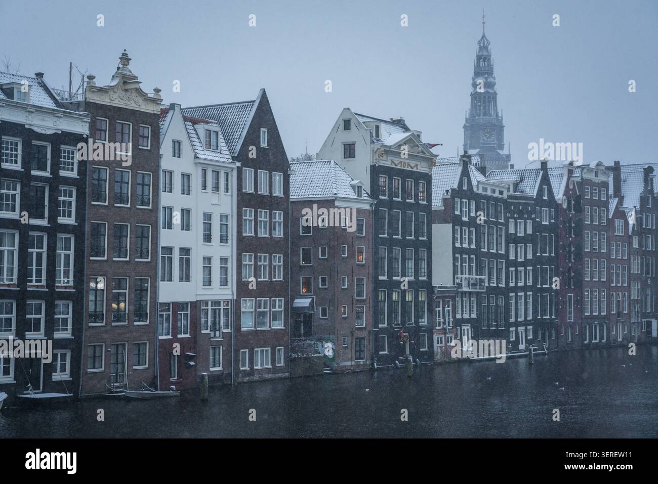 Ein malerischer Blick auf historische Grachtenhäuser entlang eines ruhigen Kanals in Amsterdam, Niederlande, unter weichem Schneefall. Schneebedeckte Dächer und Fenster Stockfoto