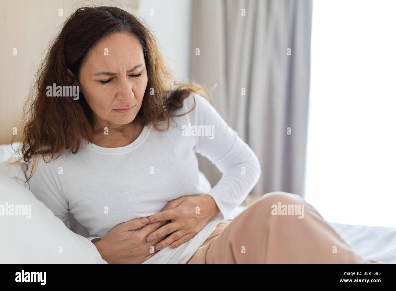 Frau, die im Bett sitzt und Bauchschmerzen hat Stockfoto