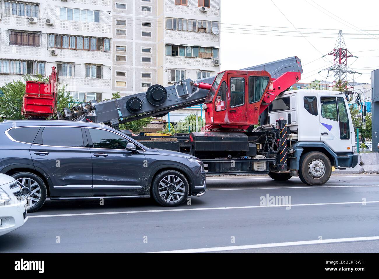 Ein mobiler Lastwagenkran, der mitten im Verkehr auf einer belebten Stadtstraße fährt. Konzept: Instandhaltung der städtischen Infrastruktur, schwere Maschinen und zivile Logistik Stockfoto