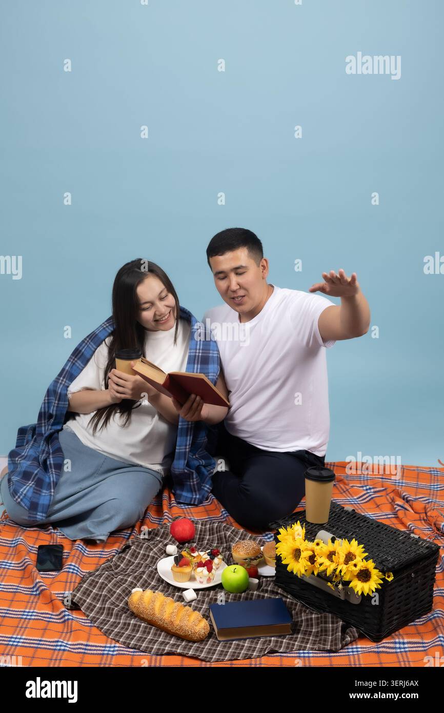 Ein Paar, das ein Picknick macht und ein Buch auf blauem Hintergrund liest Stockfoto