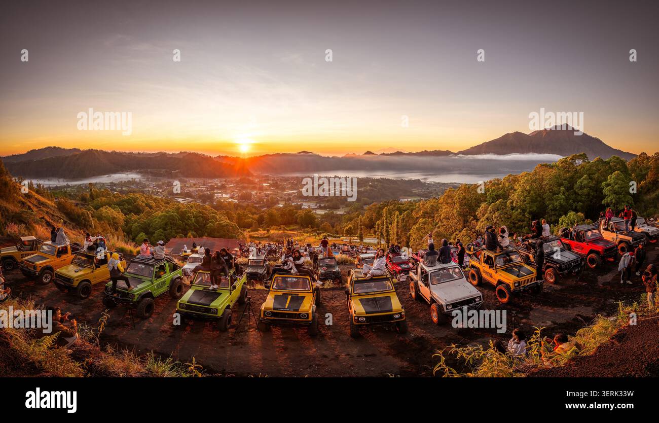 Bali, Indonesien - 2. Juni 2026: Sonnenaufgang über dem Mount Batur in Kintamani, Bali, mit farbenfrohen Geländejeeps, die an einem malerischen Aussichtspunkt auf dem Vulkan geparkt werden. Eine bestellung Stockfoto
