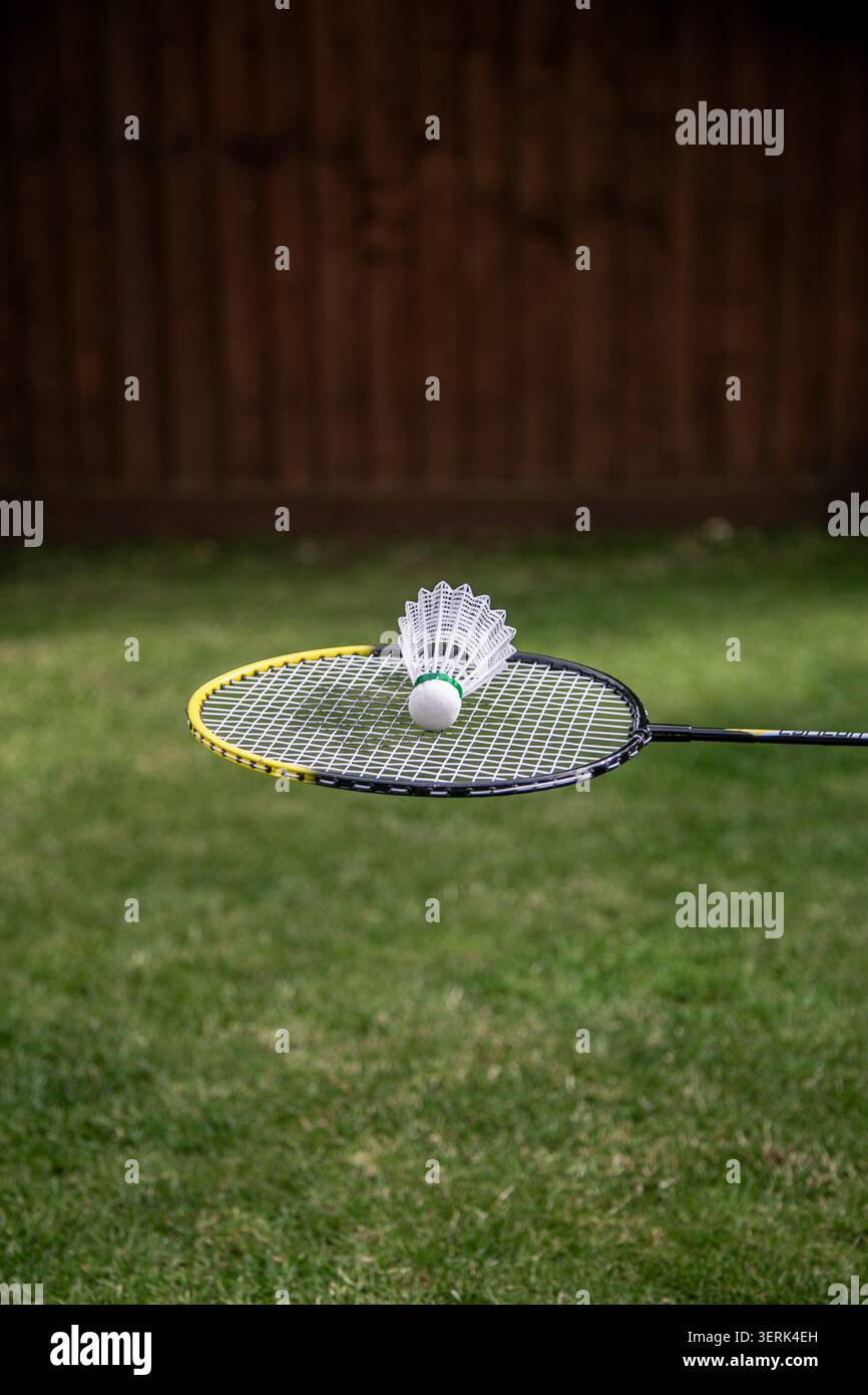 Badmintonschläger mit einem synthetischen Shuttlecock, der auf seinen Fäden liegt und über einem grünen Rasen gehalten wird. Das Bild zeigt Badminton-Ausrüstung im Freien Stockfoto