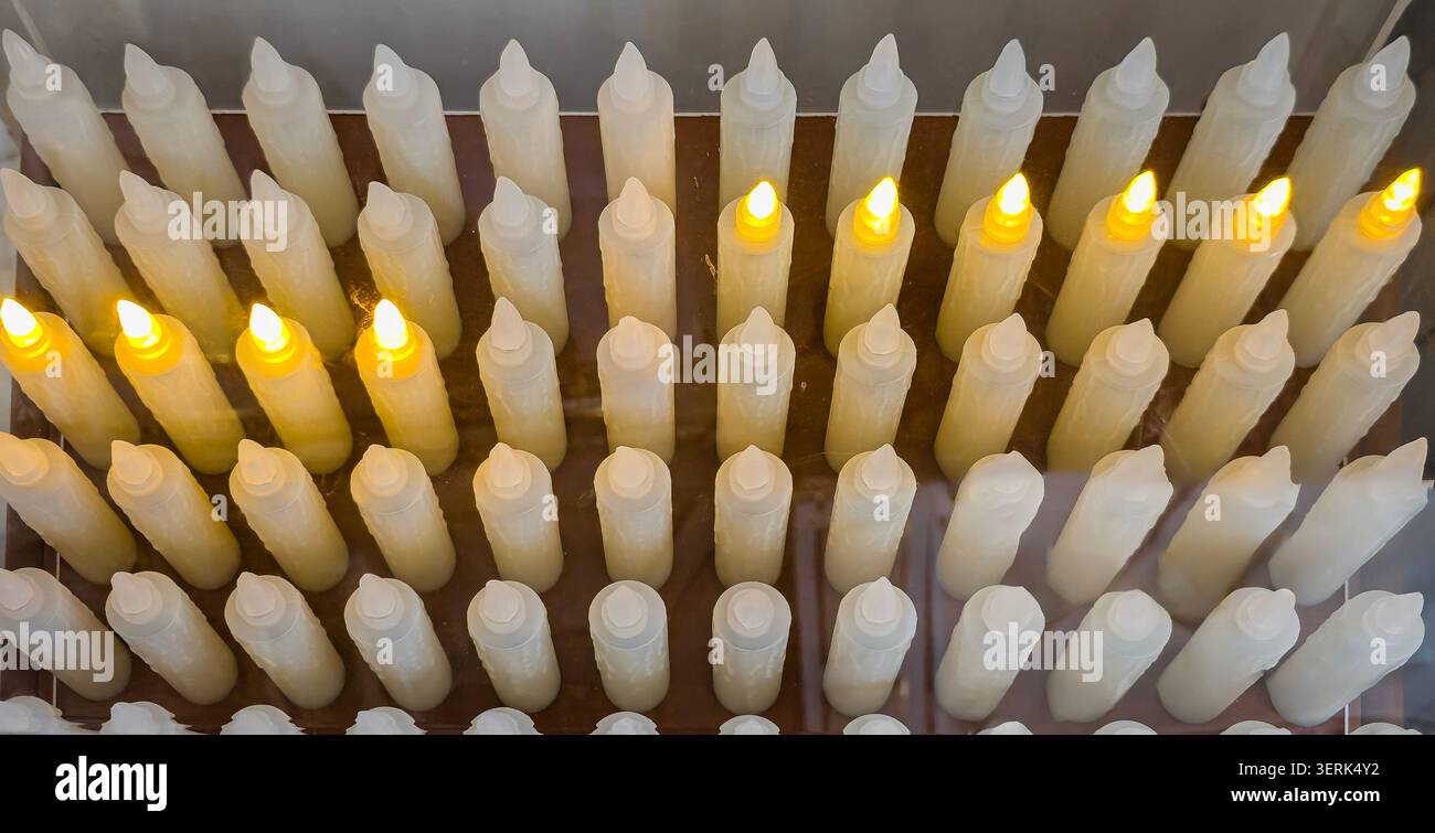 Viele elektronische weiße LED-Wachskerzen ohne Flammen stehen in einer Reihe und leuchten jeweils in warmgelbem Licht. Die Anordnung bildet ein einfaches und einheitliches Muster Stockfoto