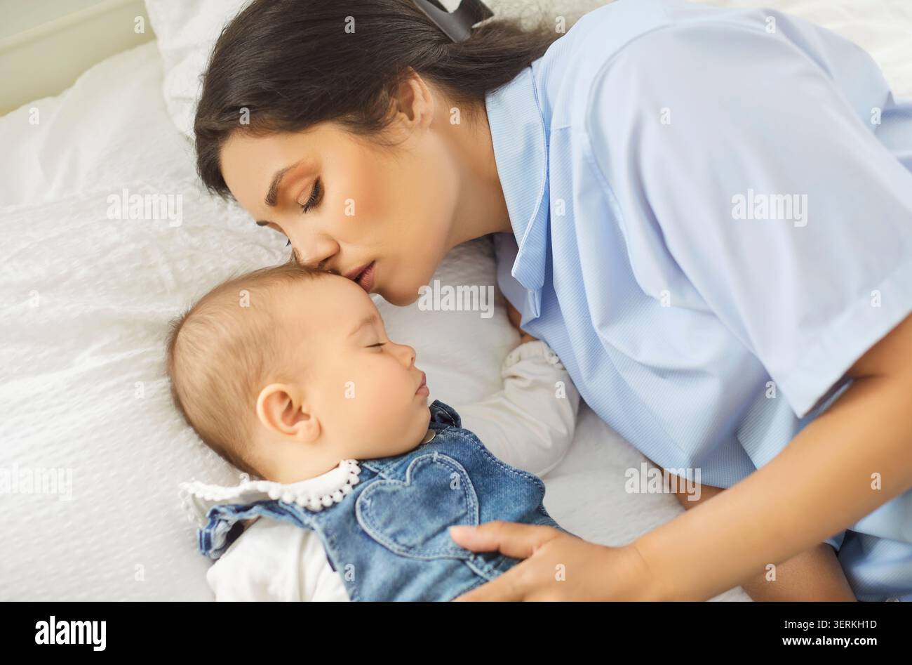 Mutter küsst schlafendes Baby auf einem weißen Bett, zärtlich kuschelt und pflegt Bindung Stockfoto