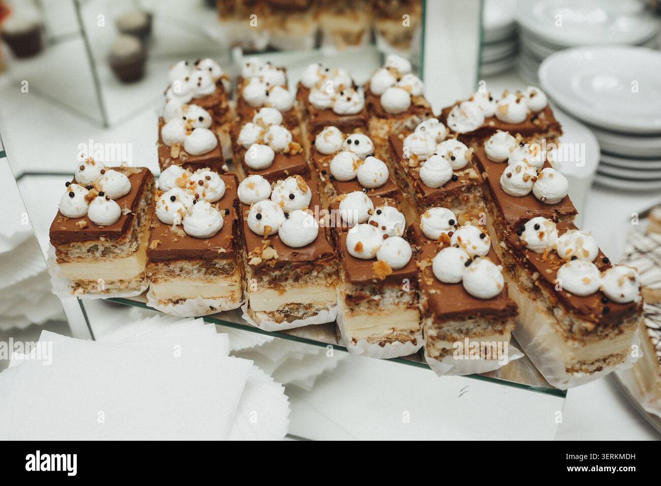 Delikater Schokoladen-Mousse-Kuchen mit Sahne- und Zuckergarnituren. Reihen süßer Köstlichkeiten sitzen auf einem Glastablett. Zierliche weiße Baisons krönten jedes quadratische dess Stockfoto