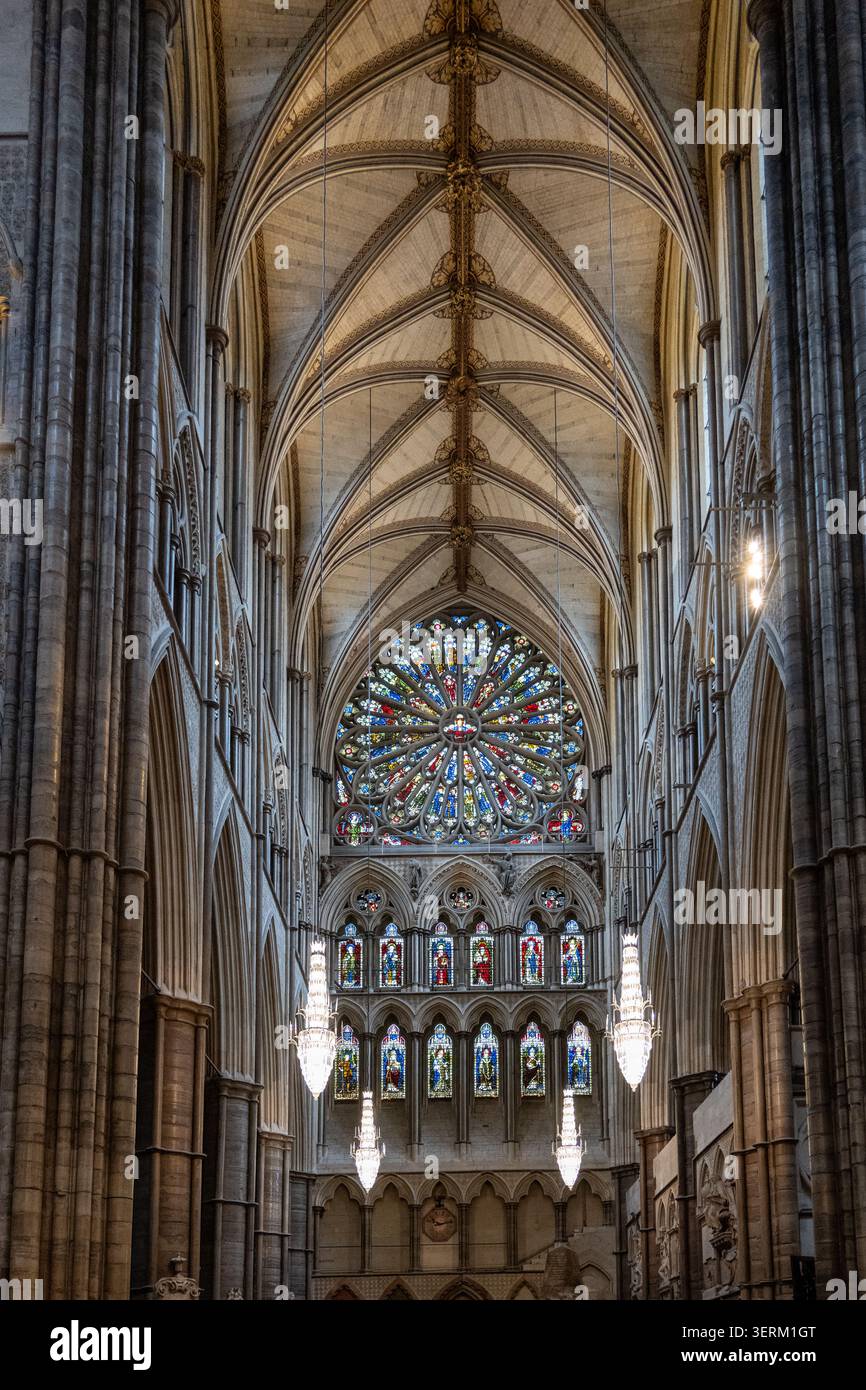 Vertikale Ansicht des gotischen Kirchenschiffs in Westminster Abbey mit Rippengewölben, Steinsäulen, hängenden Kronleuchtern und einem Buntglasrosenfenster in Londo Stockfoto