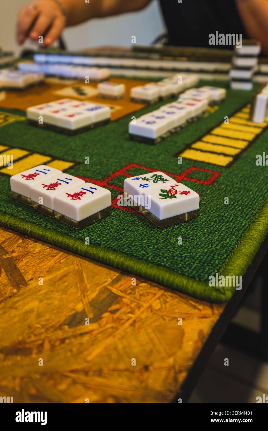 Ein Mahjong-Spiel, das auf einer grünen Matte im Vordergrund freigelegte Figuren- und Blumenkacheln zeigt. Stockfoto