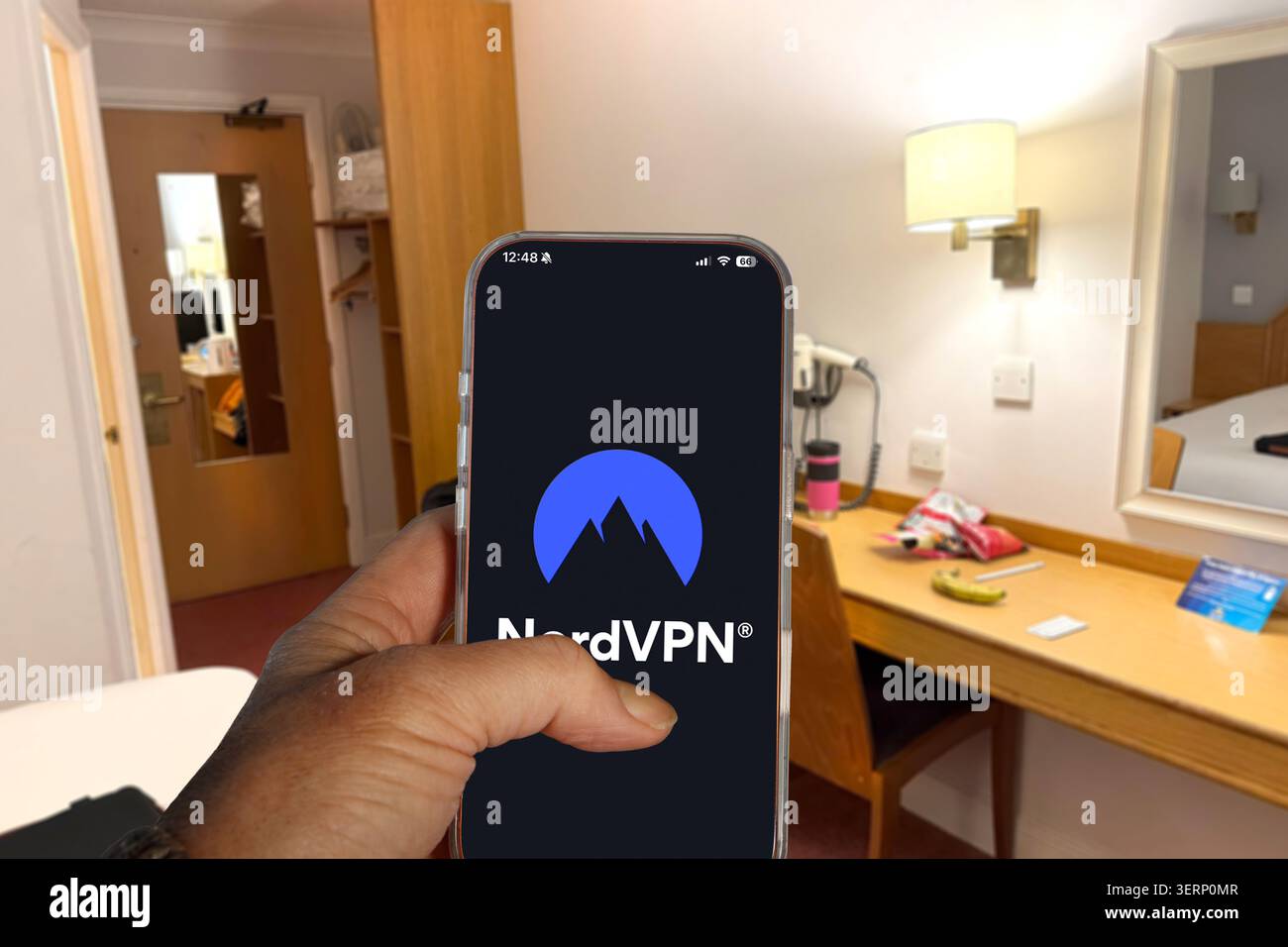 Halten Sie ein iPhone mit dem NordVPN-Logo auf dem Bildschirm in einem Hotelzimmer Stockfoto