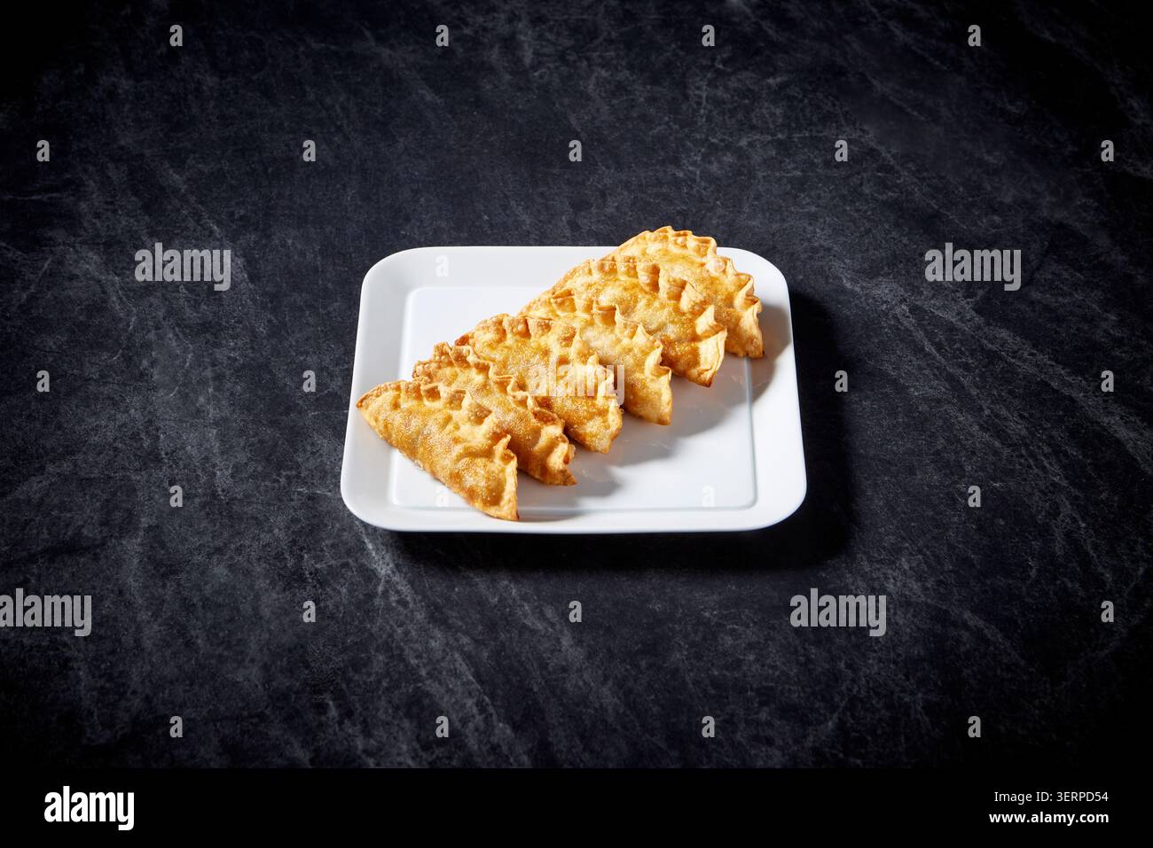 Gebratene chinesische Klößchen Gyoza serviert auf einem weißen quadratischen Teller auf dunklem Steinhintergrund, Nahaufnahme Lebensmittelfotografie Stockfoto