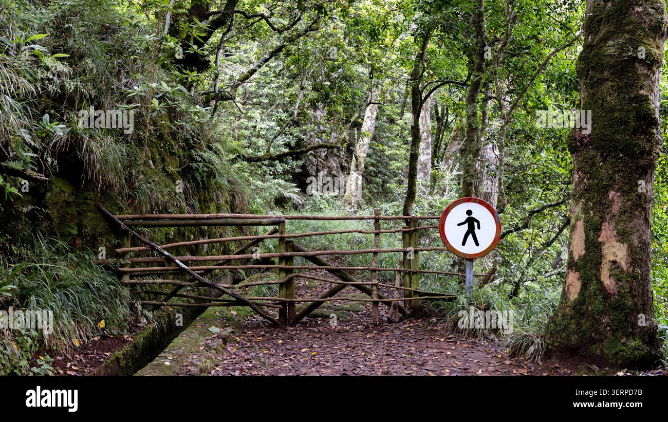 Eine Touristenroute entlang einer Levada auf Madeira, Portugal, blockiert durch ein Tor mit einem Schild für den Nichteinstieg. Tropische Vegetation. Stockfoto