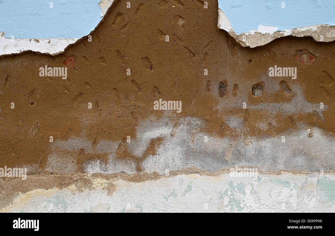Horizontale Nahaufnahme einer verwitterten, verrotteten Wandoberfläche mit abblätternder blauer Farbe, gerissener weißer Farbe, abgenutztem Beton, Terrakotta-Schicht Stockfoto
