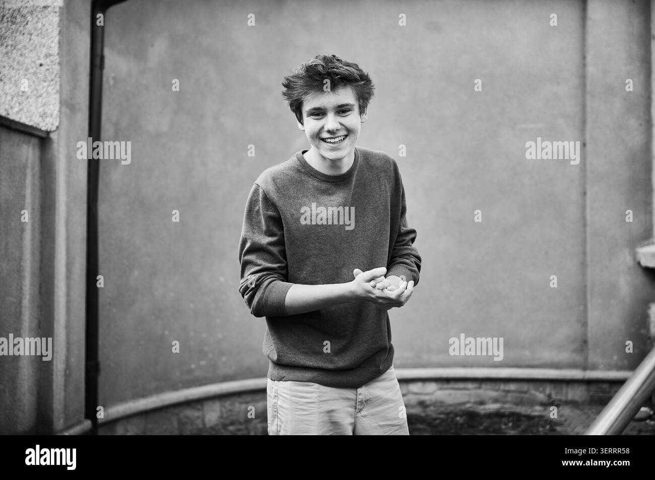 Teenager lächelt draußen in die Kamera, Schwarzweiß-Porträt in urbaner Umgebung mit Betonwand Hintergrund. Für den Jugendstil, positive Emotionen, Selbstvertrauen, Bildung oder redaktionelle Zwecke Stockfoto