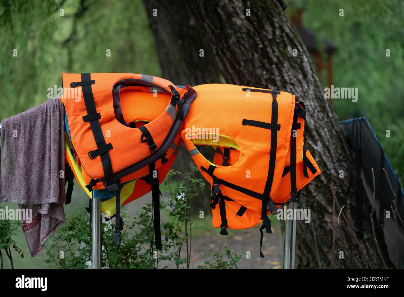 Leuchtend orange Schwimmwesten trocknen auf einem Gestell im Freien in der Nähe eines Baumes. Detaillierte Nahaufnahme von orangen persönlichen Schwimmhilfen mit schwarzen Bändern auf einem Rücken Stockfoto