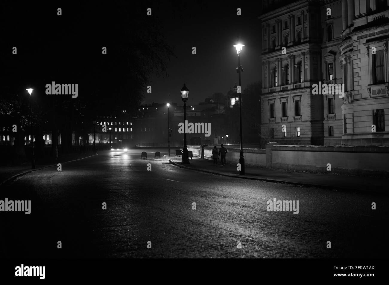 Schwarzweißbild der Horse Guards Road bei Nacht mit altmodischer Straßenbeleuchtung und Pärchen zu Fuß Stockfoto