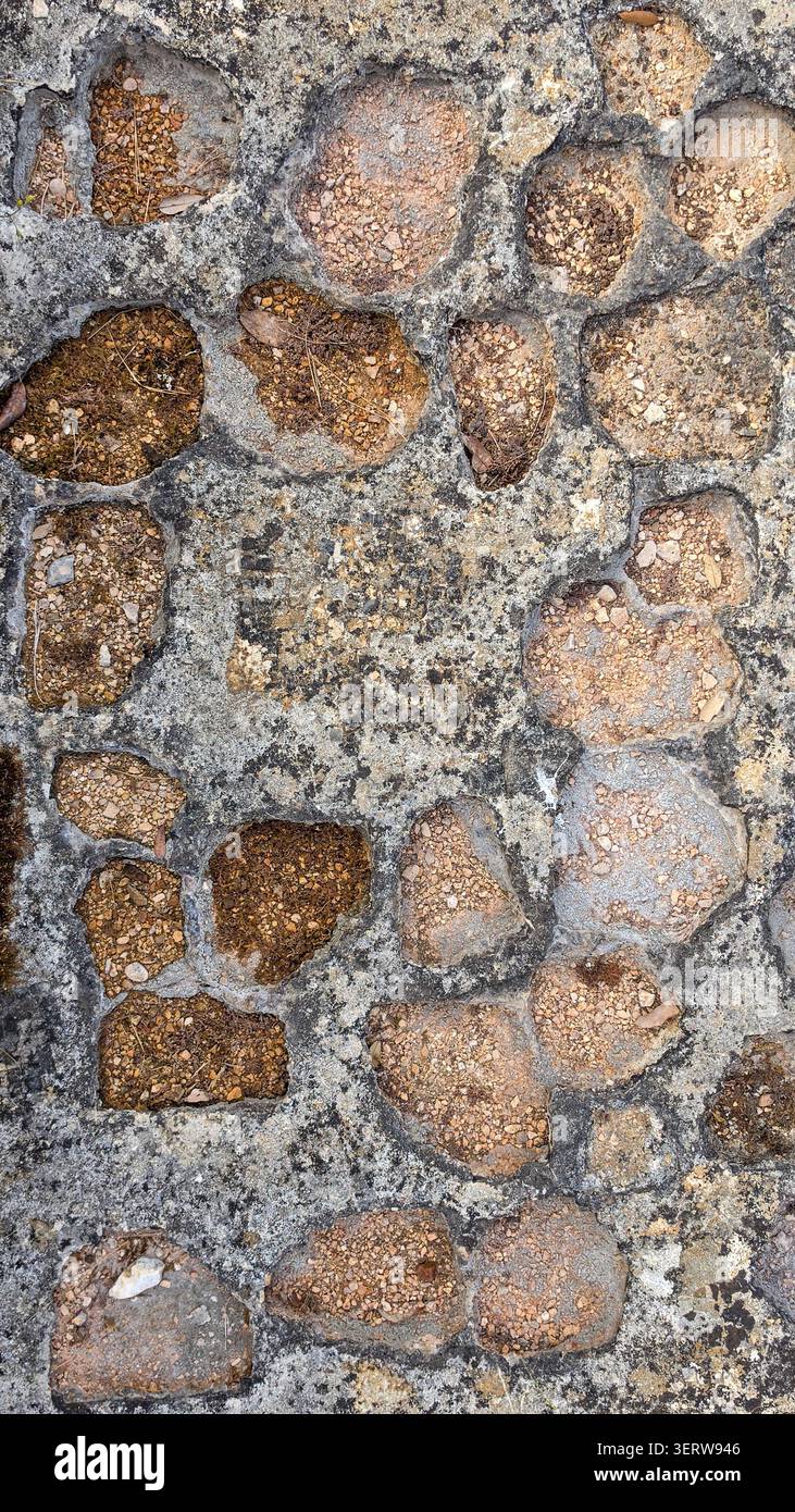Nahaufnahme von unregelmäßigen Natursteinpflastersteinen, die in einem strukturierten Muster mit Boden, kleinen Felsen und getrockneten Blättern in den Spalten liegen und das Wetter zeigen Stockfoto