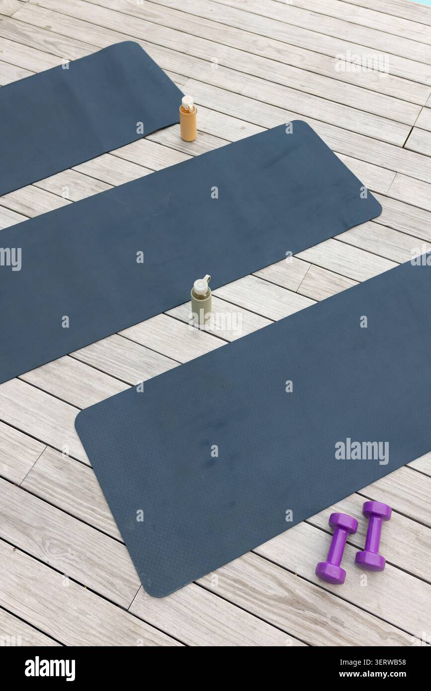 Die mittlere schieferblaue Trainingsmatte liegt schräg auf Holzdeck, mit Flaschen und lila Gewichten Stockfoto
