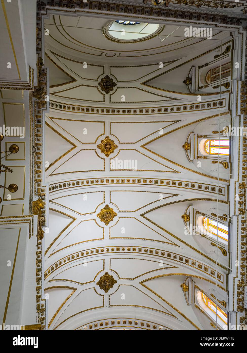 Das Innere einer weißen Kathedrale hat eine Decke mit gerippten Gewölben. Goldene Medaillons befinden sich entlang der Decke und gewölbte Kirchenfenster l Stockfoto