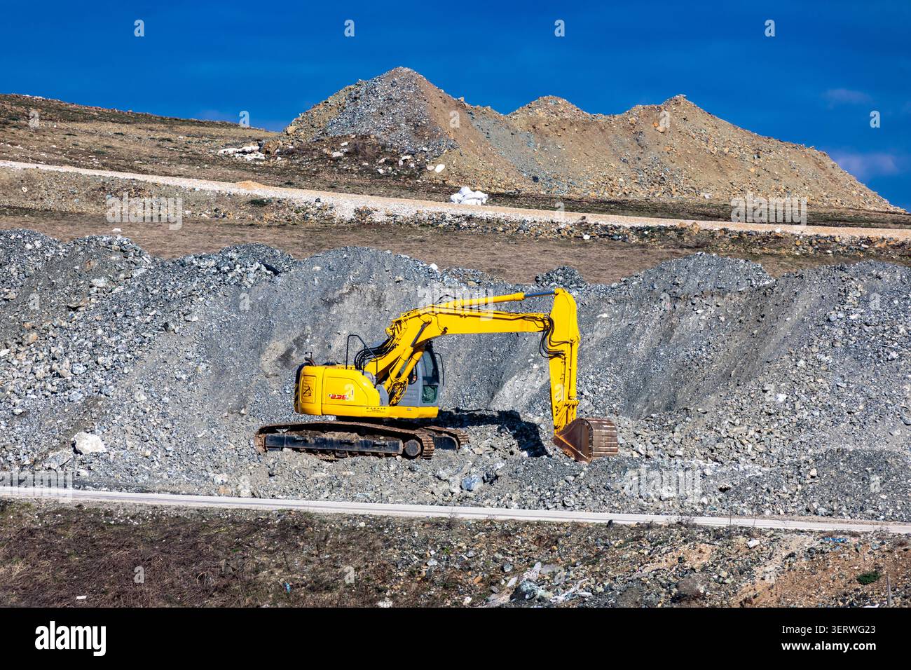 ZLATIBOR, SERBIEN – 05. April 2026: Ein gelber Bagger arbeitet auf einem Kieshaufen auf einem offenen Bergbaugelände unter hellblauem Himmel. Die Maschine befindet sich in Position Stockfoto