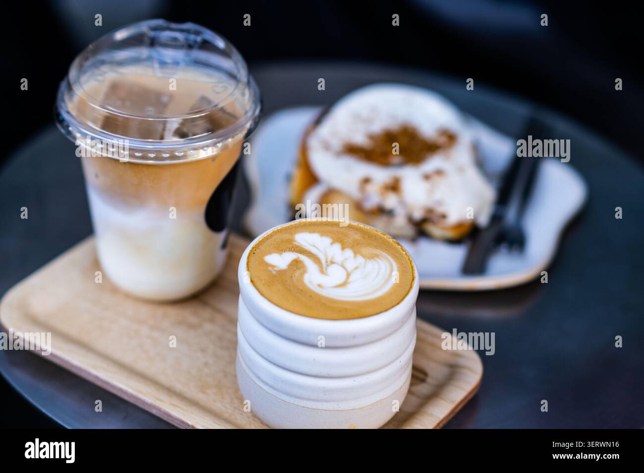 Eine gemütliche Kaffeepausen-Szene mit einem Latte mit komplizierten Schaumkunstwerken, einem Eiskaffee und einem Teller mit mit Zimt bestäubten Pfannkuchen. Stockfoto