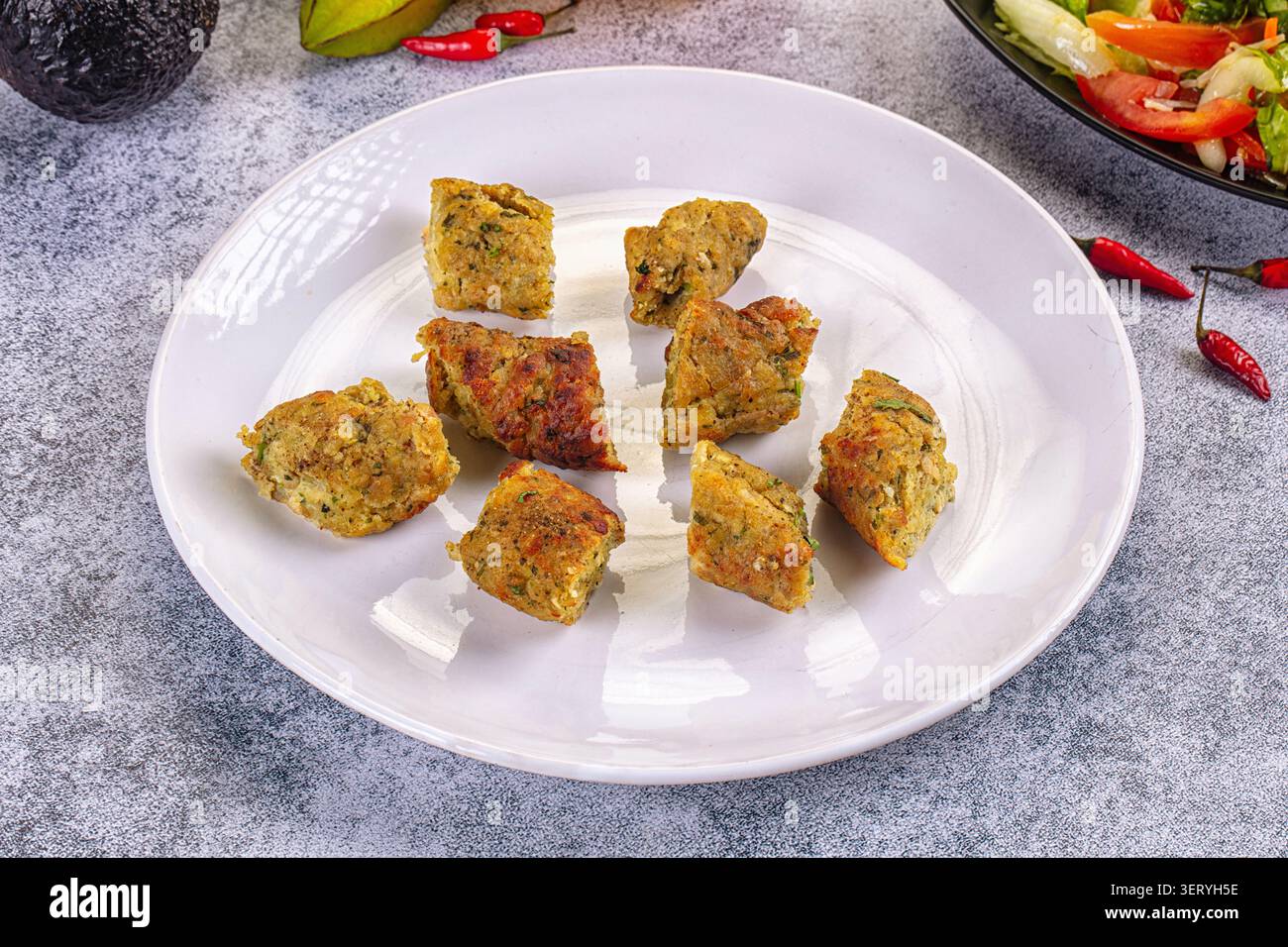 Über dem Kopf geschossen neun goldbraune herzhafte Krapfen angeordnete weiße Platte. Frische Avocado, Sternfrucht, roter Chili-Paprika Hintergrund. Helles, einladendes Studio Stockfoto