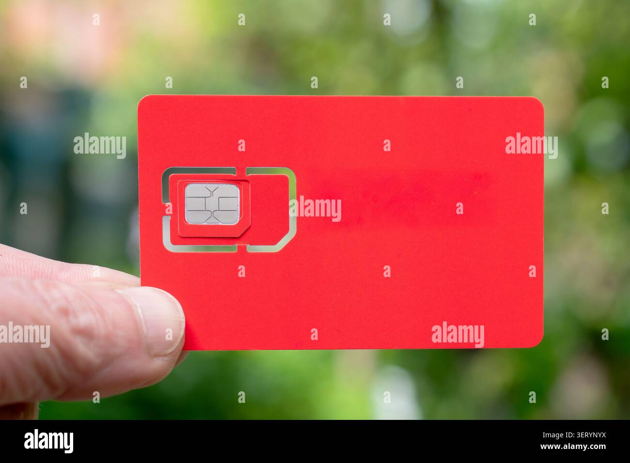 Halten Sie einen roten sim-Kartensteckplatz gegen eine unscharfe grüne Einstellung für den Außenbereich. Aktivieren der Mobilfunkkommunikation. Nahaufnahme. Stockfoto