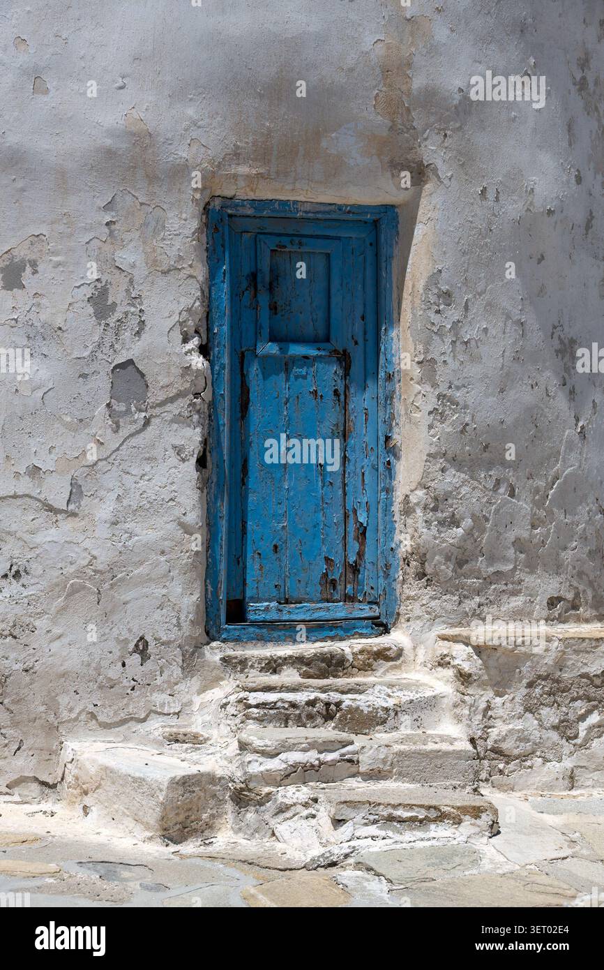 Alte blaue Holztür mit abblätternder Farbe in der weißen Wand mit Stufen Stockfoto