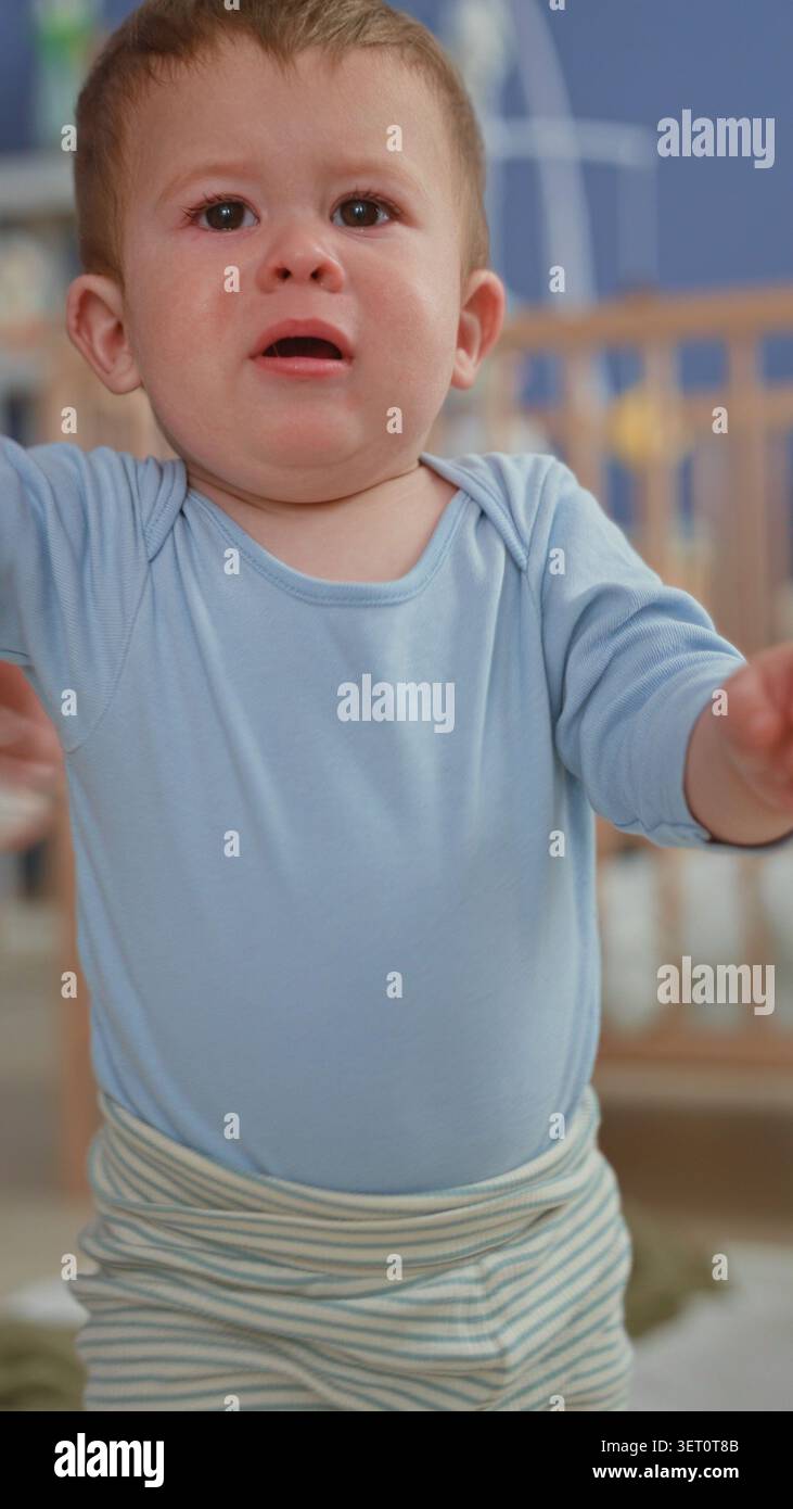 Der Junge weint und greift nach einem Spielzeug, während sich die Pflegekraft in einem Gebäude mit einem Taschentuch das Gesicht abwischt. Stockfoto