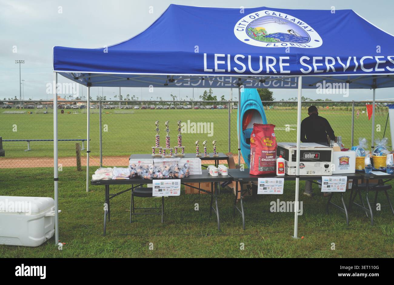 Panama City, FL, USA. Juni 2026. Trophäen, Geschenkkörbe und ein pelikanisches Kajak in blaugrün das City of Callaway Leisure Services Zelt mit beleuchteten Ballfeldern dahinter beim 23. Jährlichen Callaway Children's Fishing Rodeo. Das kostenlose Vatertag-Wochenende steht Teilnehmern bis 16 Jahren in Begleitung eines Erwachsenen offen. Fish Florida spendete den ersten 200 Kindern kostenlose Ruten- und Walzenkombinationen, mit Verlosungspreisen, kostenlosen Hot Dogs und Trophäen, die für den größten Fisch und die längste Besetzung vergeben wurden. Quelle: Tosh Persons / Alamy Live News Stockfoto