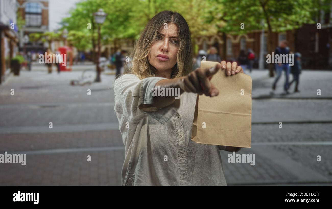 Eine Frau, die eine Papiertüte hält, zeigt den Finger auf einer belebten Straße mit einem angespannten Gesicht und einem ausgedehnten Finger nach vorne; eine durchsetzungsfähige Forderung. Stockfoto