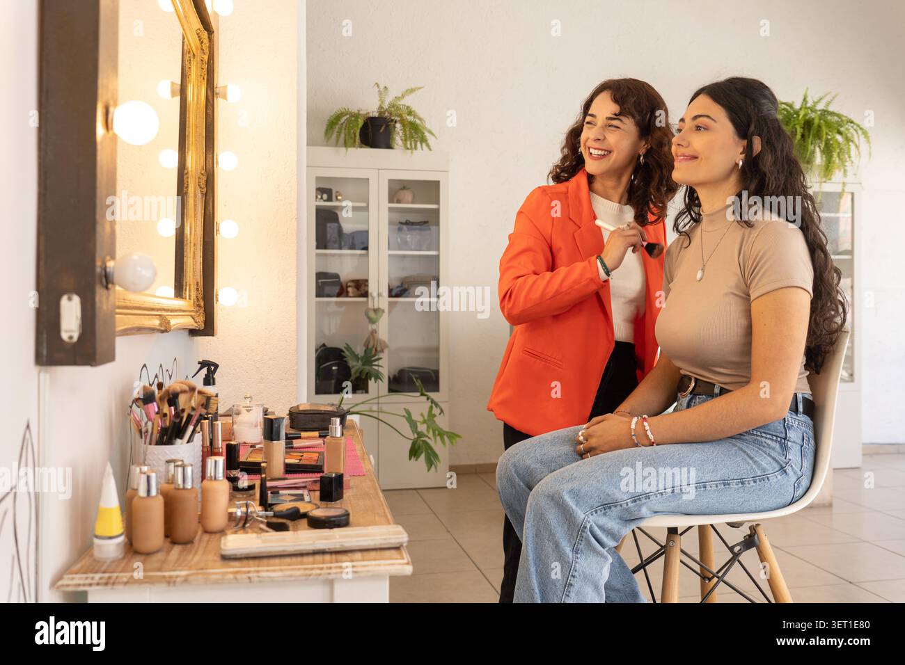 Make-up-Künstler und Kunde teilen sich einen freudigen Moment und lachen gemeinsam nach einer abgeschlossenen Make-up-Sitzung in einem hellen Schönheitssalon. Stockfoto
