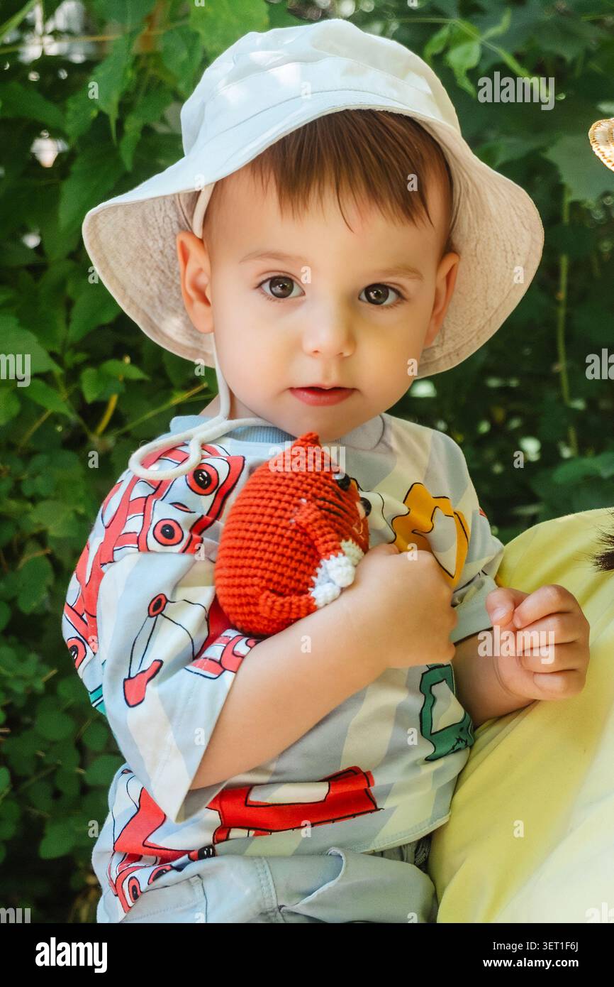 Kleinkind mit Sonnenhut, das im Freien gehäkeltes Spielzeug hält Stockfoto