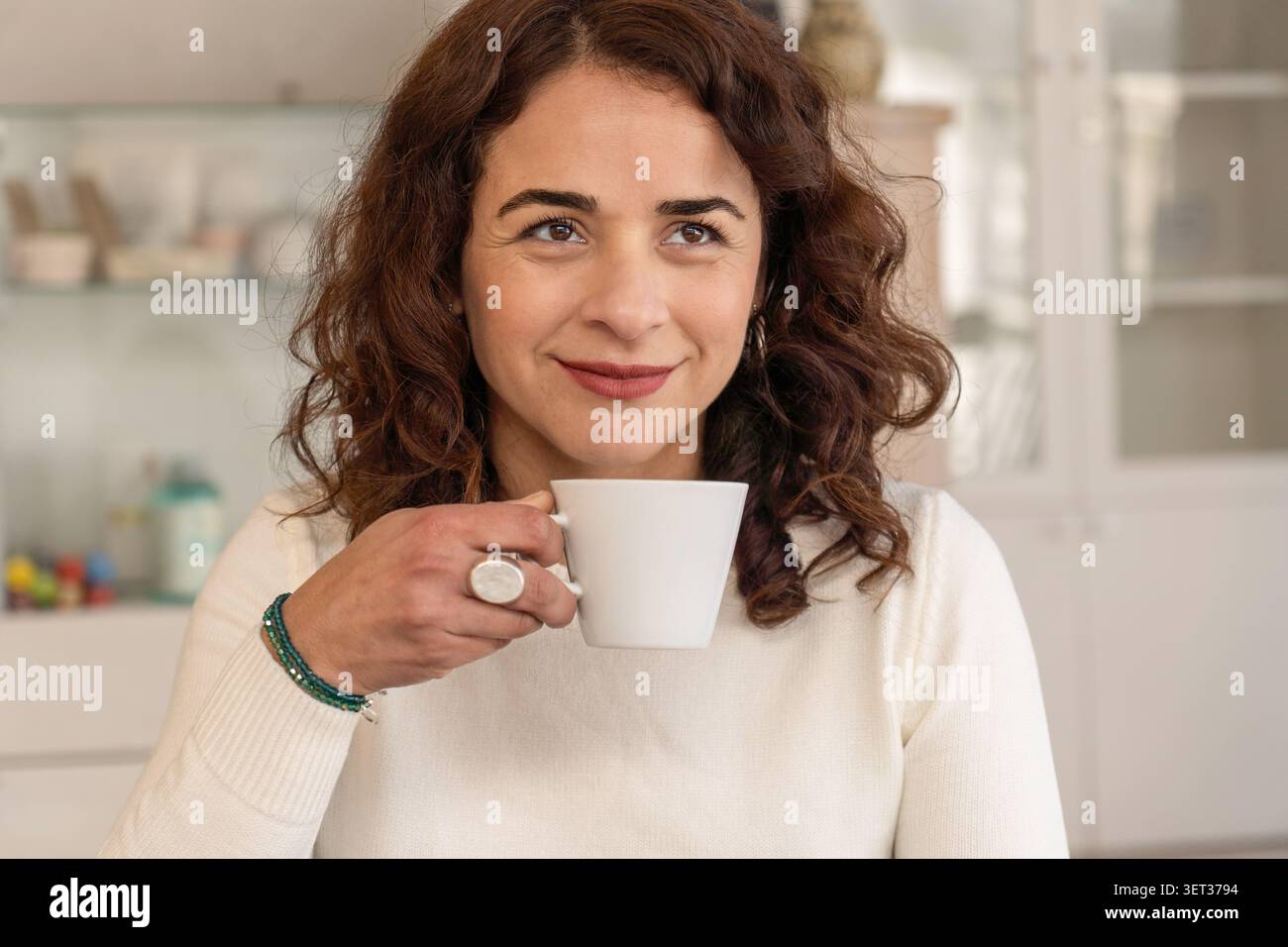 Porträt einer selbstbewussten Frau mittleren Alters, die in einer entspannten professionellen Umgebung eine Kaffeetasse hält und die Kamera anlächelt. Stockfoto