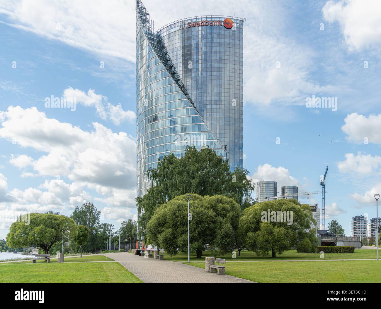 Städtisches Wachstumsgleichgewicht. Swedbank Büroturm umgeben von landschaftlich gestalteten öffentlichen Räumen in Riga, Lettland, spiegelt das Zusammenleben von moderner Entwicklung und uriger Entwicklung wider Stockfoto