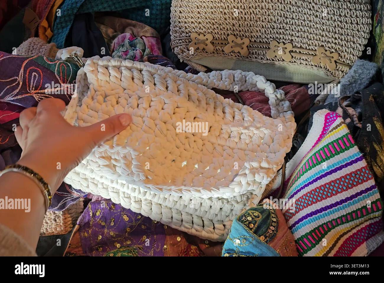 Eine Person hält eine weiße gehäkelte Handtasche neben anderen bunten Stoffgegenständen. Stockfoto