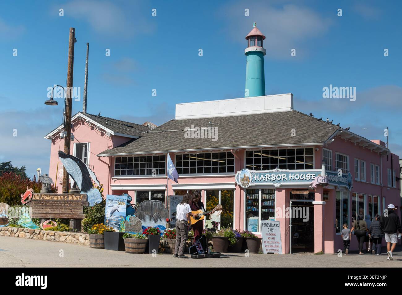 Monterey, CA, 6. Juni 2026. Ein Musiker tritt auf der Straße vor dem Harbor House in Monterey auf. Die Sonne scheint auf das farbenfrohe Gebäude. P Stockfoto