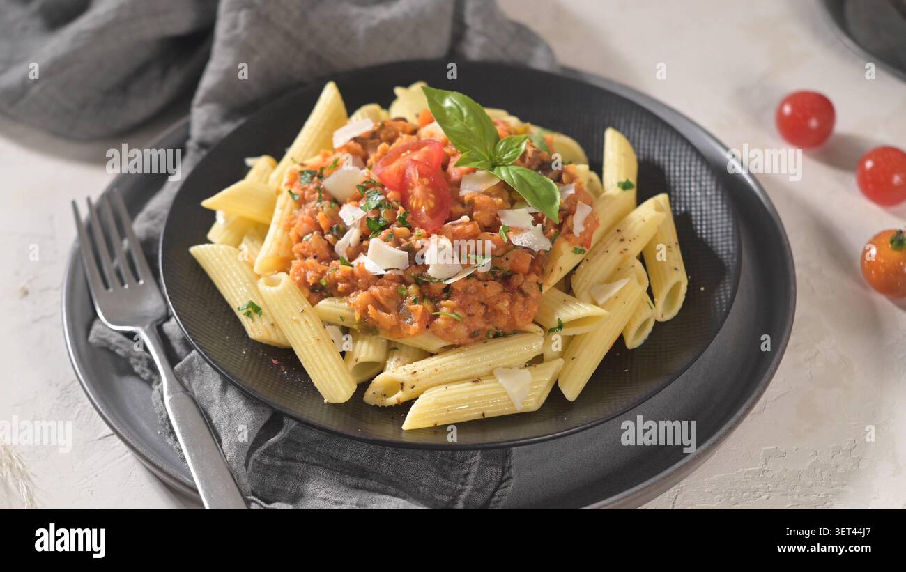 Dieses herzhafte Gericht umfasst perfekt gekochte Penne-Pasta, die mit einer reichhaltigen Tomaten- und Linsensauce überzogen ist. Serviert auf einem dunklen Teller, die lebhaften Farben und frisch Stockfoto