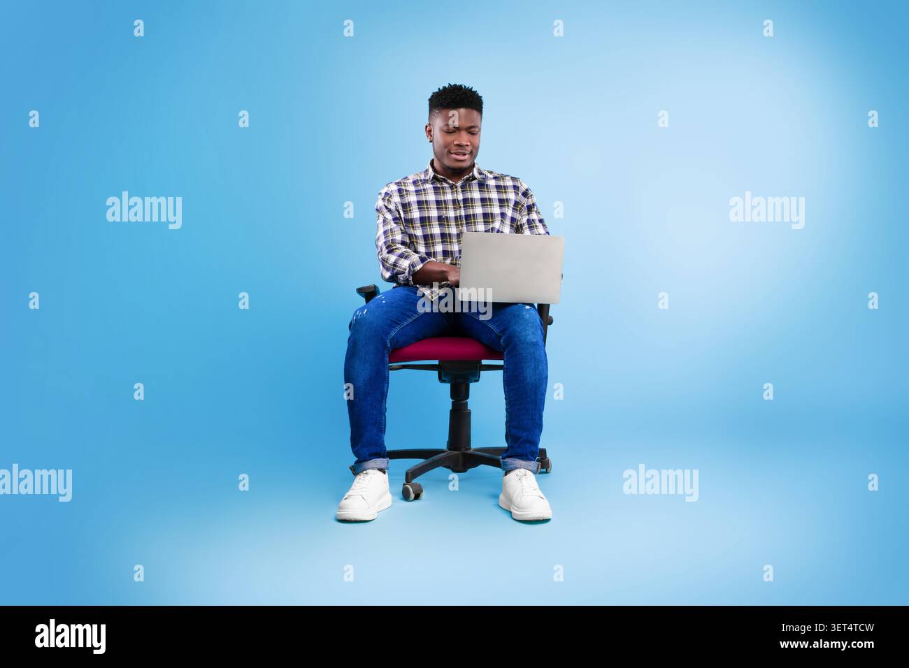 Junger Afroamerikanischer Mann, Der Am Laptop Arbeitet, Während Er Auf Dem Bürostuhl Sitzt, Business Concept Stockfoto