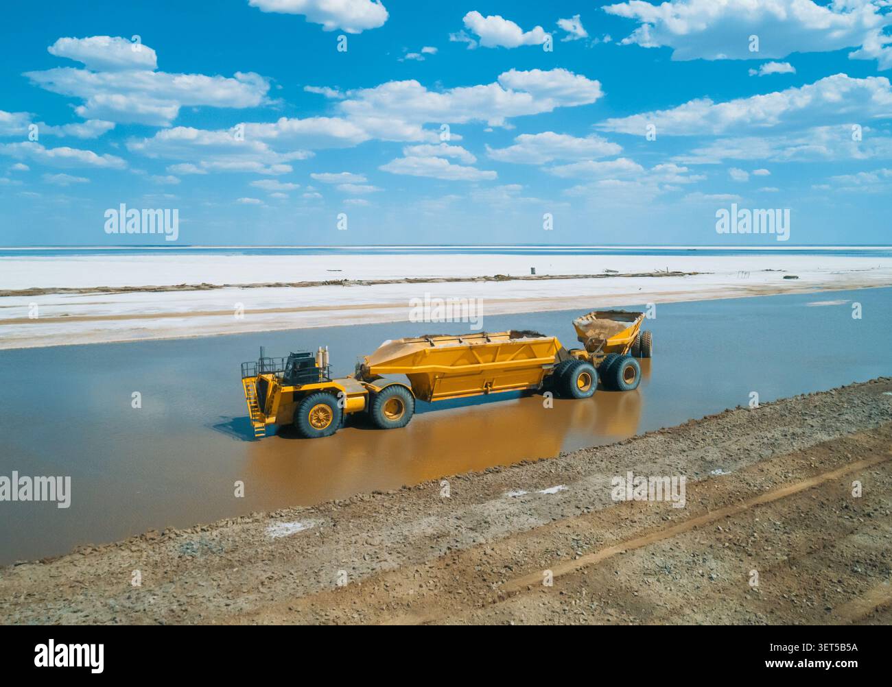 Ein großer gelber Lkw fährt in einem Salzbergbaugebiet und transportiert Mineralien über nassen Boden. Stockfoto