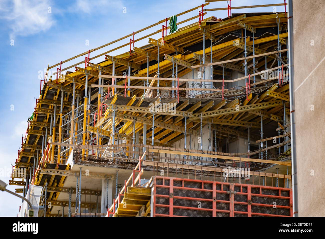Eine detaillierte Perspektive auf ein mehrstöckiges Appartementgebäude im Bau mit komplexen Gerüstgerüsten und hellgelber Bausubstanz Stockfoto