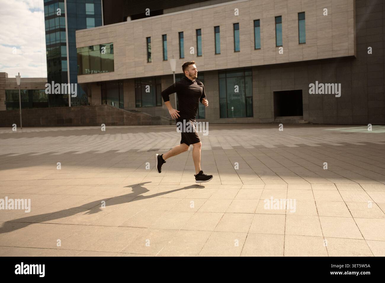 Mann joggt auf einem urbanen Pfad mit moderner Architektur im Hintergrund während des Tages Stockfoto