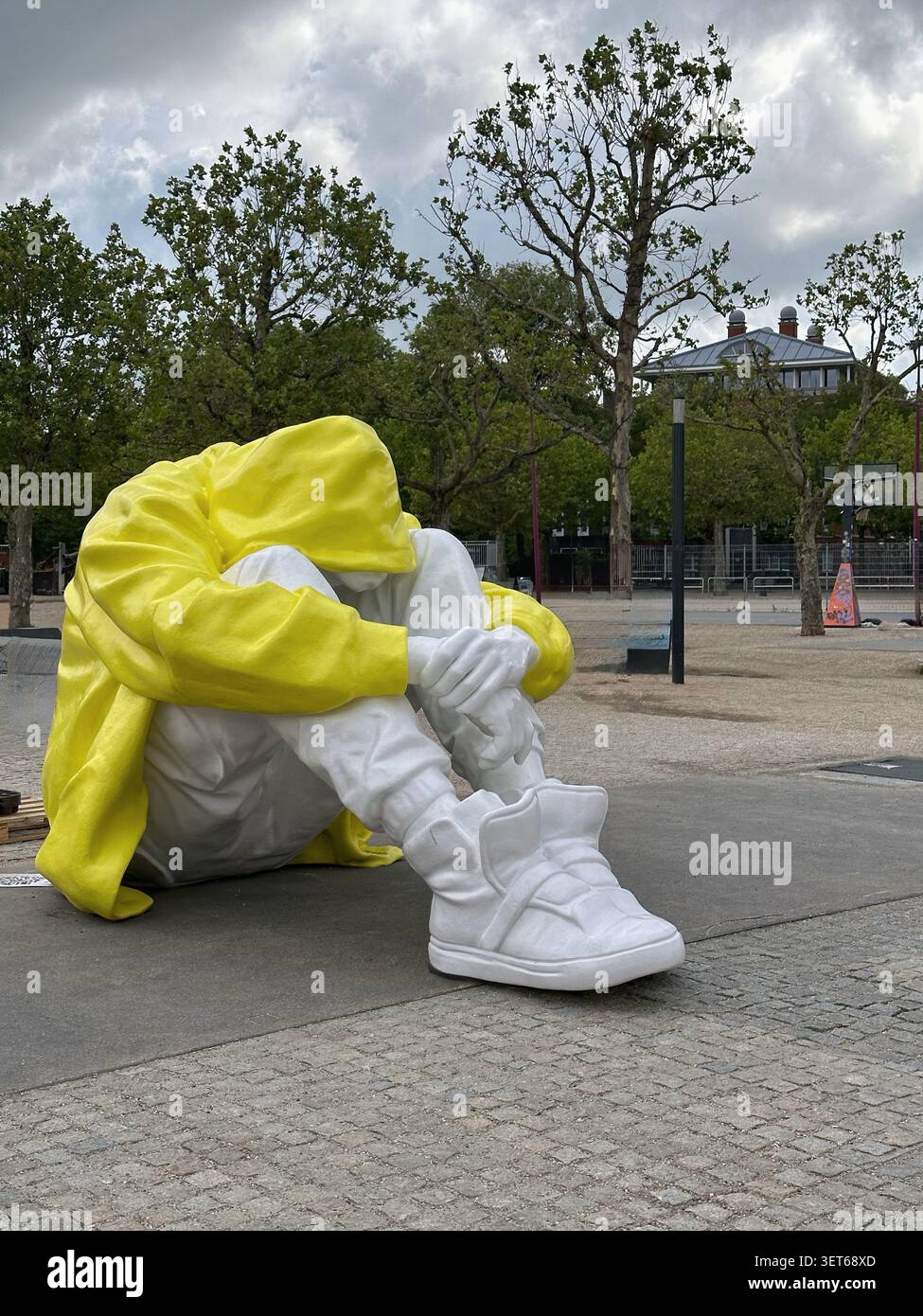 Eine große zeitgenössische öffentliche Kunstinstallation, die eine überzogene Person darstellt. Die gesichtslose Statue steht auf dem Bürgersteig eines Stadtparks mit grünen Bäumen - Smartphone-aufgenommenes Stockfoto